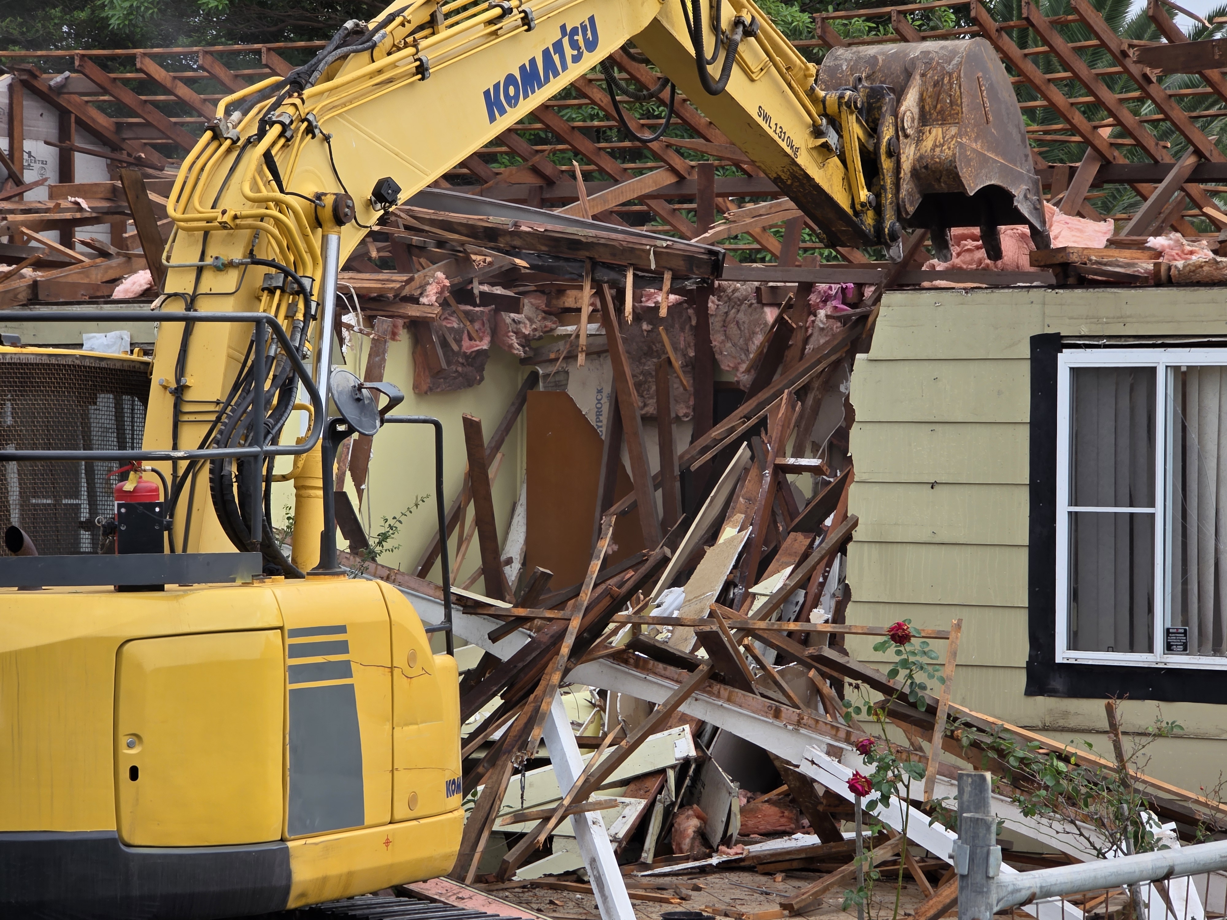 Excavator carrying out demolition of residential house.